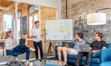 Four men sitting in a planning session with a whiteboard 