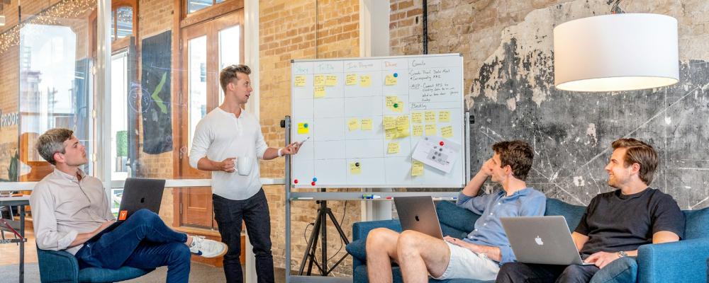 Four men sitting in a planning session with a whiteboard